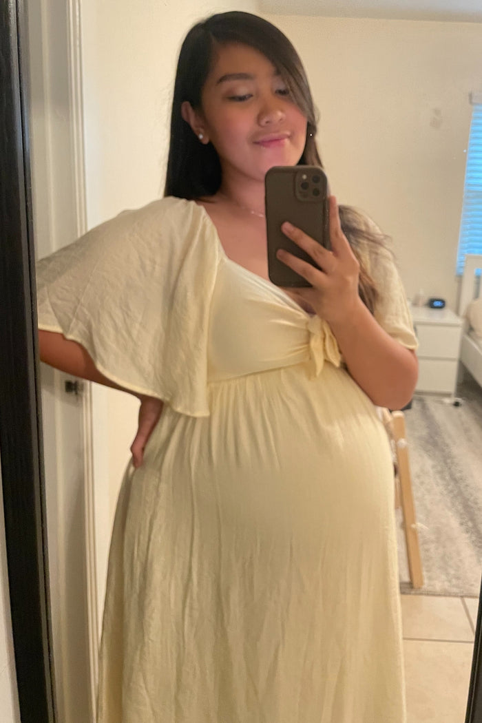 woman wearing a light yellow maternity dress with a tie detail under her bust and a visible baby bump