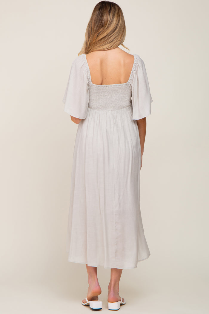 woman wearing a light gray maternity dress with flutter sleeves and a smocked bodice, showing a baby bump from the back