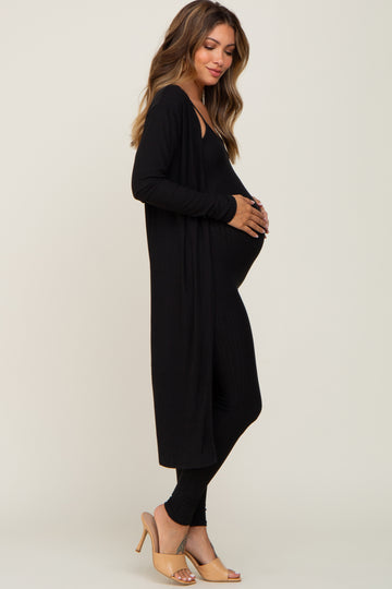 woman wearing a black long sleeve maternity cardigan over a black maternity jumpsuit and holding her baby bump