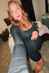 woman wearing a black maternity bodycon dress and holding her baby bump in a cozy bedroom setting