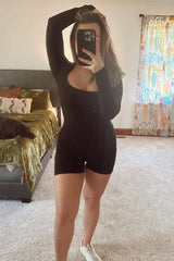 woman wearing a black long sleeve bodysuit with a scoop neckline and button details, standing in a bedroom mirror