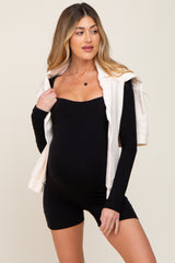 woman wearing a black maternity bodysuit with a cream zip-up hoodie draped over her shoulders and showing her baby bump
