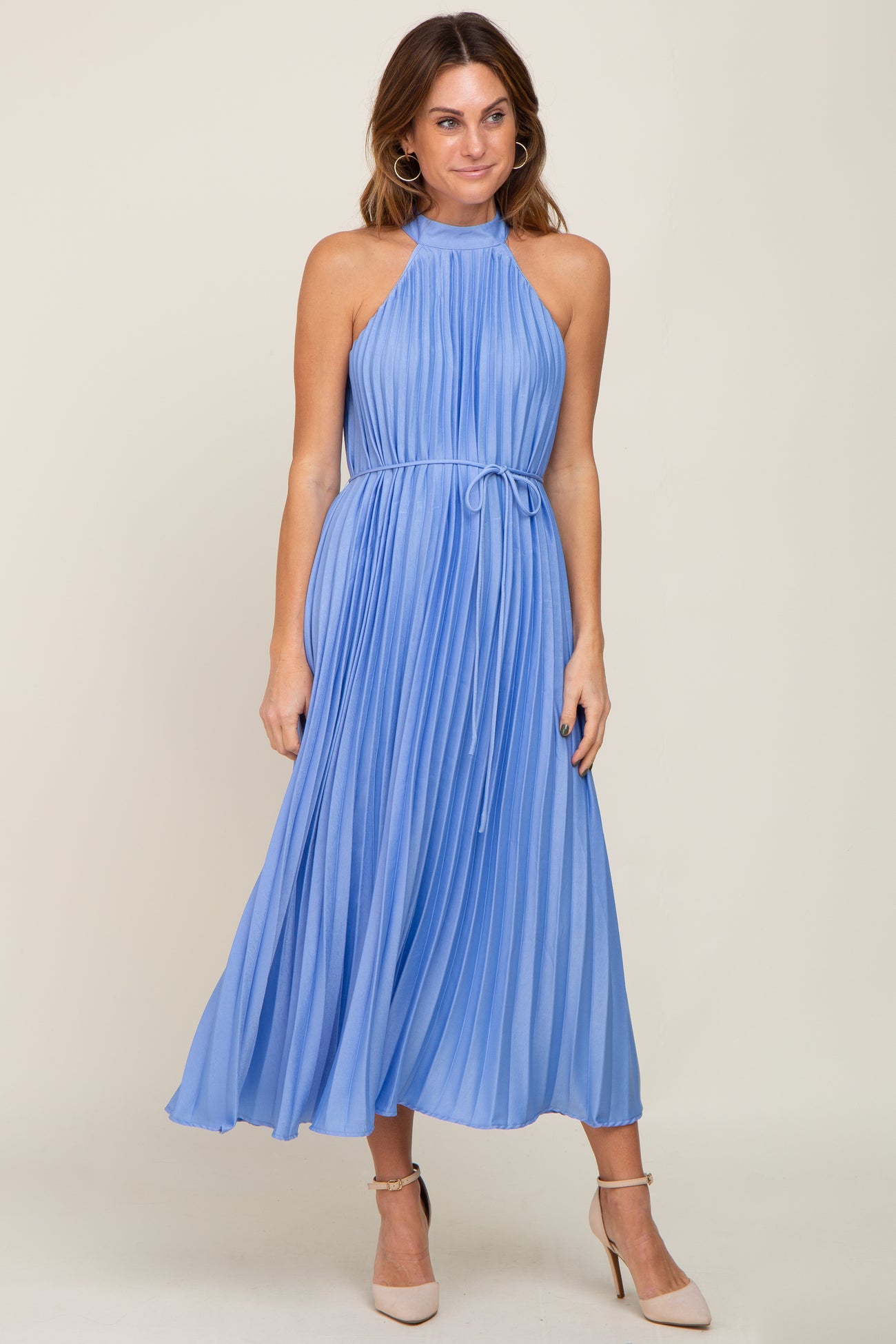 woman wearing a light blue pleated halter neck dress with a belted waist and strappy nude heels
