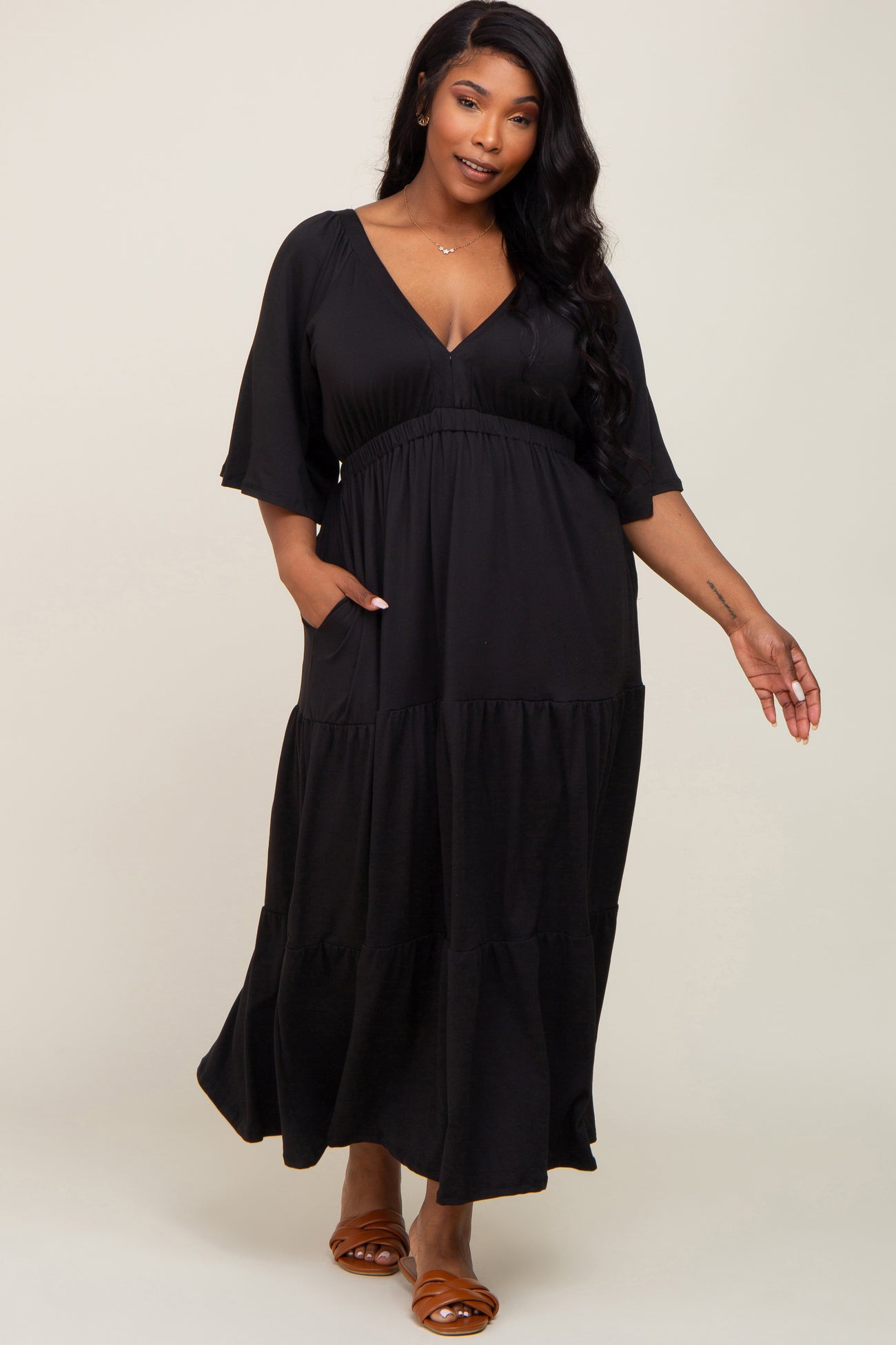 woman wearing a black tiered maxi dress with a deep v-neck and short sleeves, featuring pockets