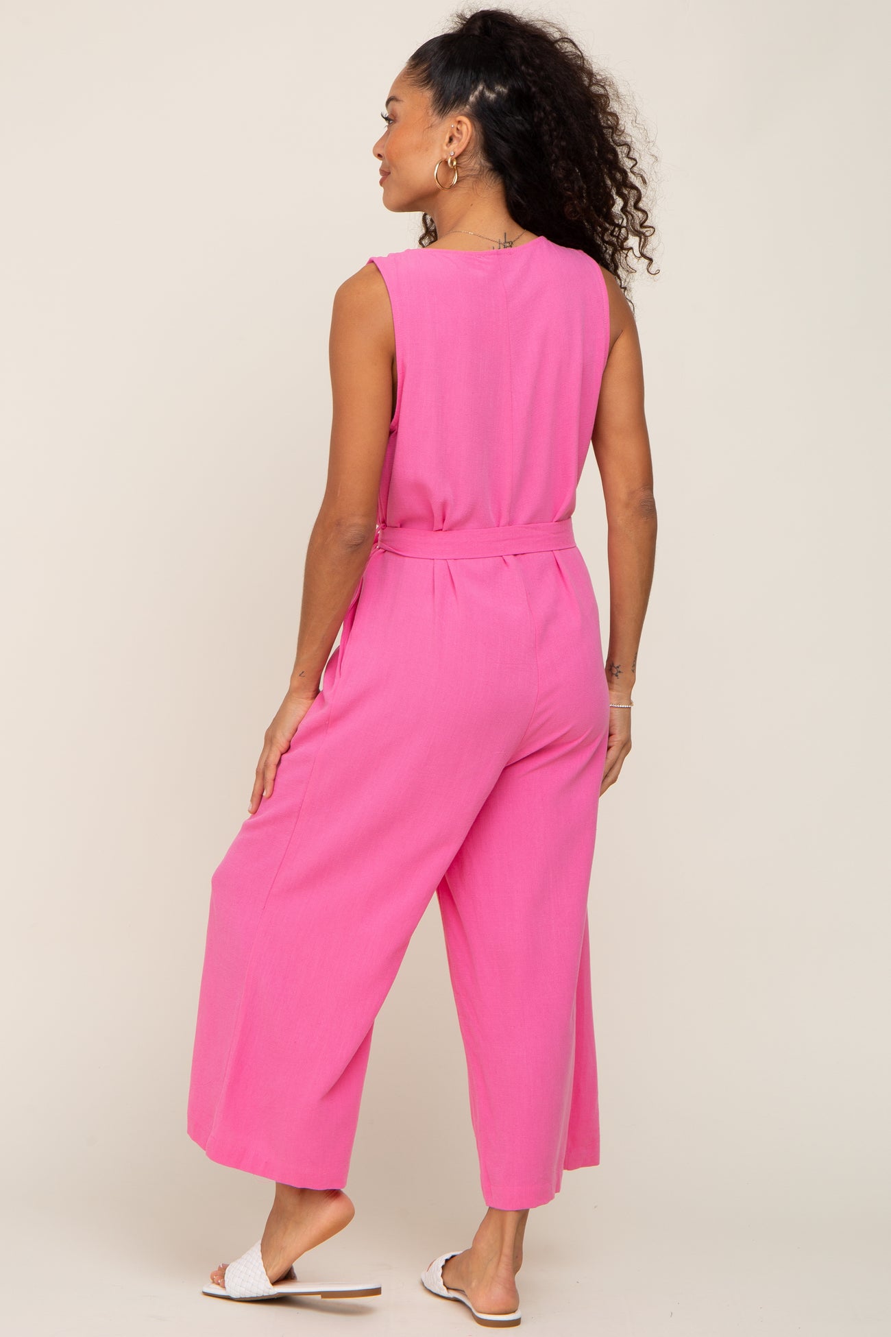 woman wearing a pink sleeveless jumpsuit with wide legs and a tie waist, viewed from the back