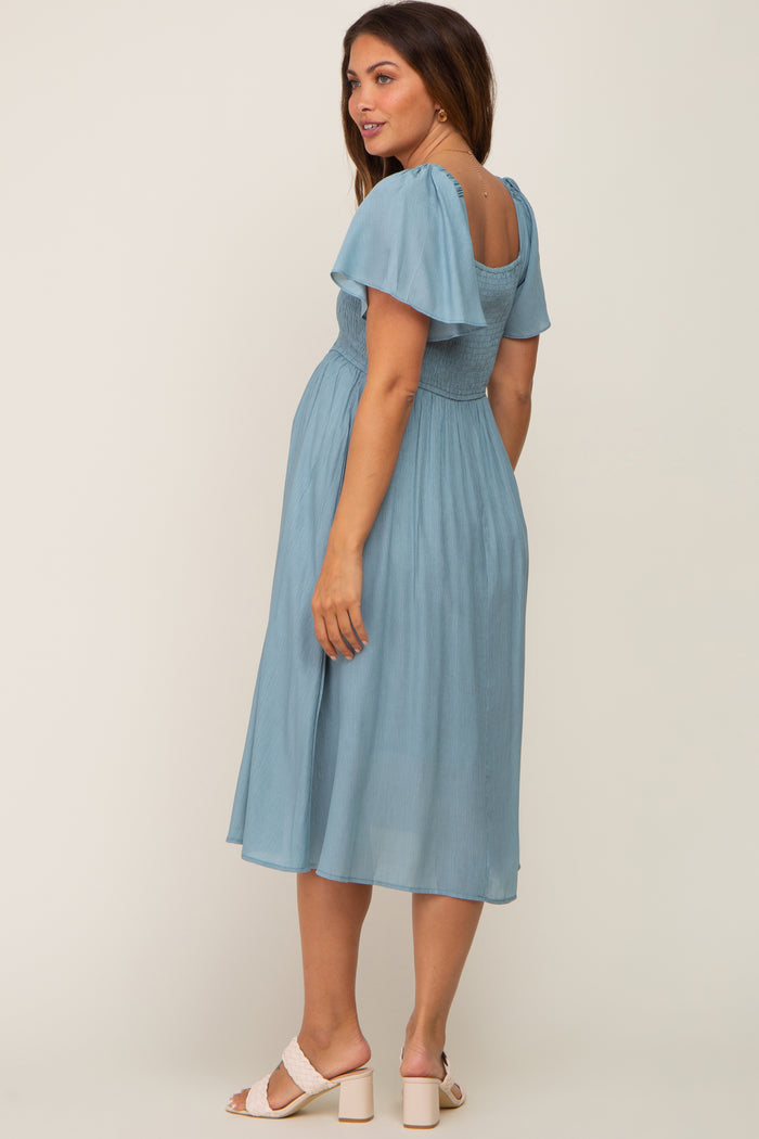 woman wearing a light blue maternity dress with flutter sleeves and a smocked bodice, showing her baby bump from the side