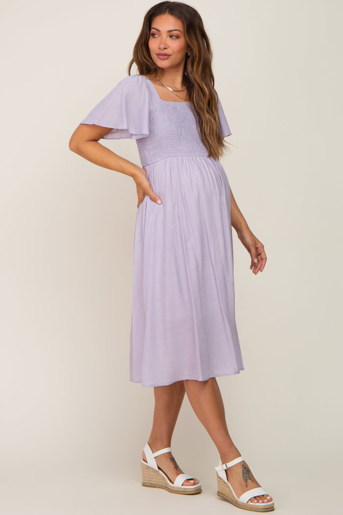 woman wearing a lavender maternity dress with short flutter sleeves and a smocked bodice, showcasing her baby bump