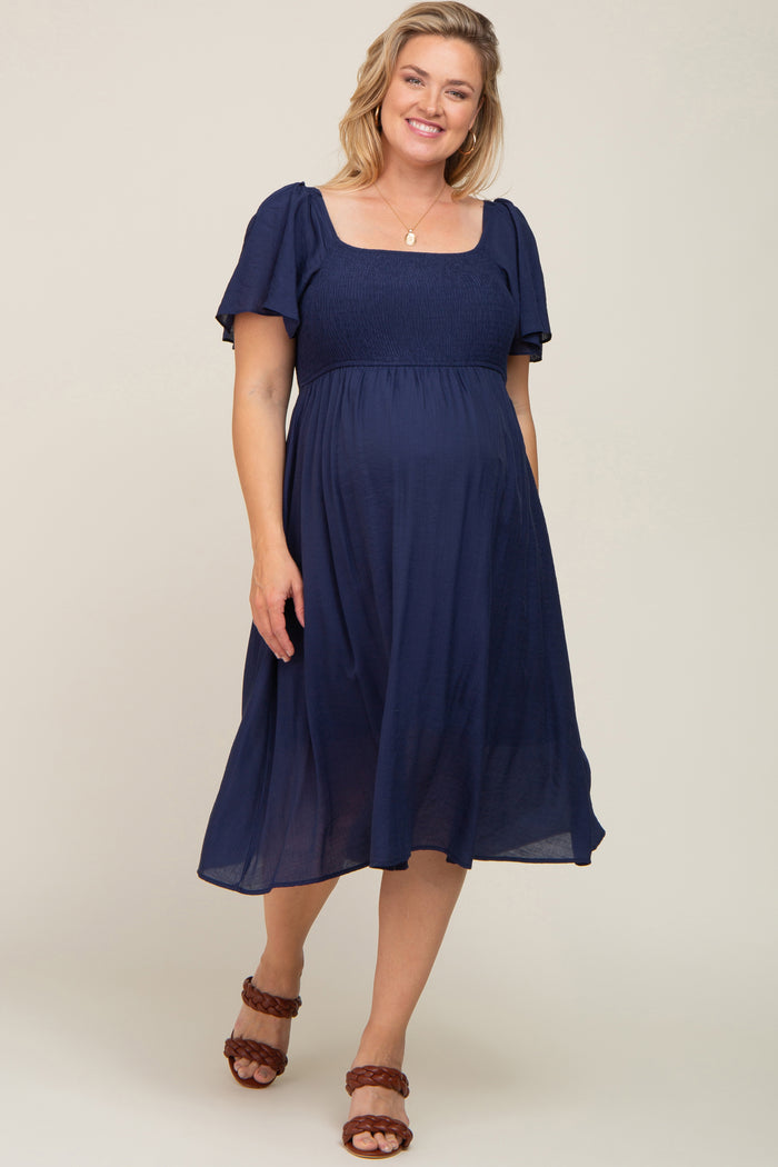 woman wearing a navy blue maternity plus dress with short puff sleeves and a smocked bodice, showcasing her baby bump