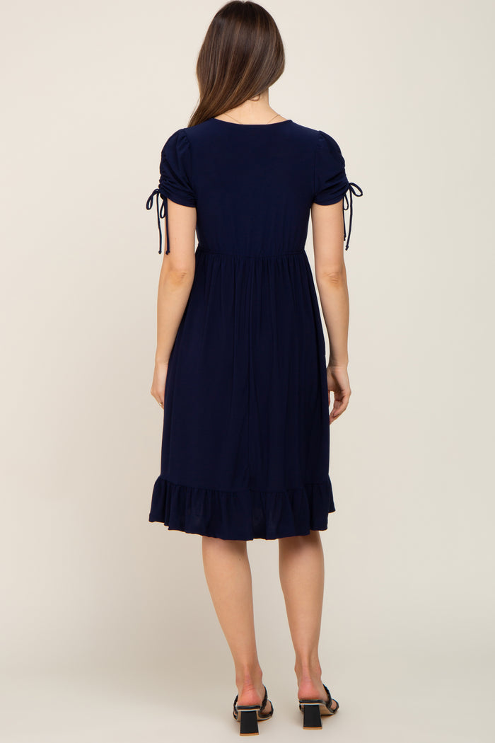 woman wearing a navy blue maternity dress with puff sleeves and tie details, featuring a ruffled hem and relaxed fit