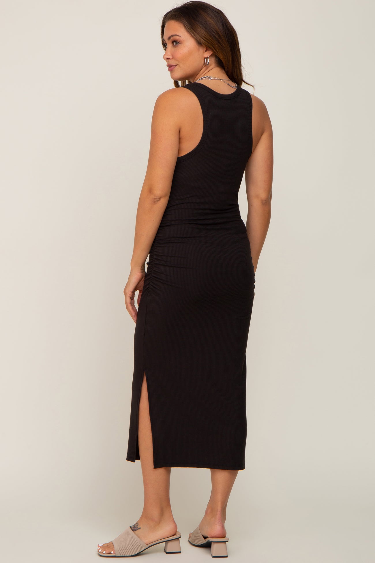 woman wearing a black ribbed maternity midi dress with side slits and a fitted silhouette
