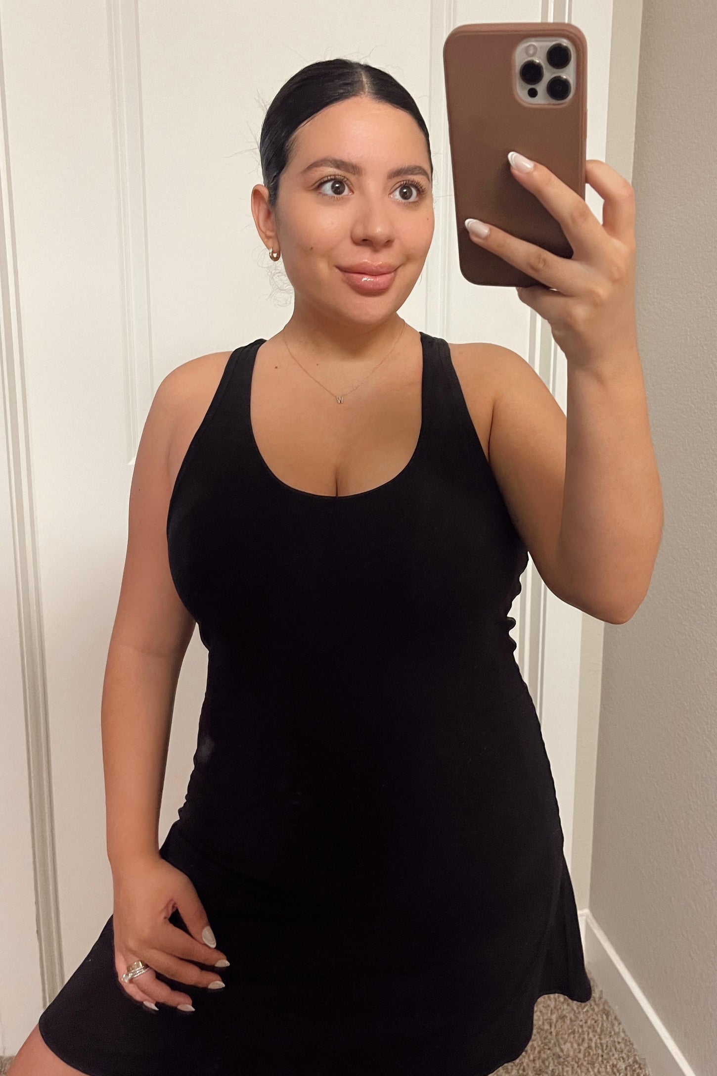woman wearing a black sleeveless dress and taking a selfie in front of a mirror