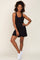 woman wearing a black sleeveless dress and white sneakers, posing with one hand on her hip