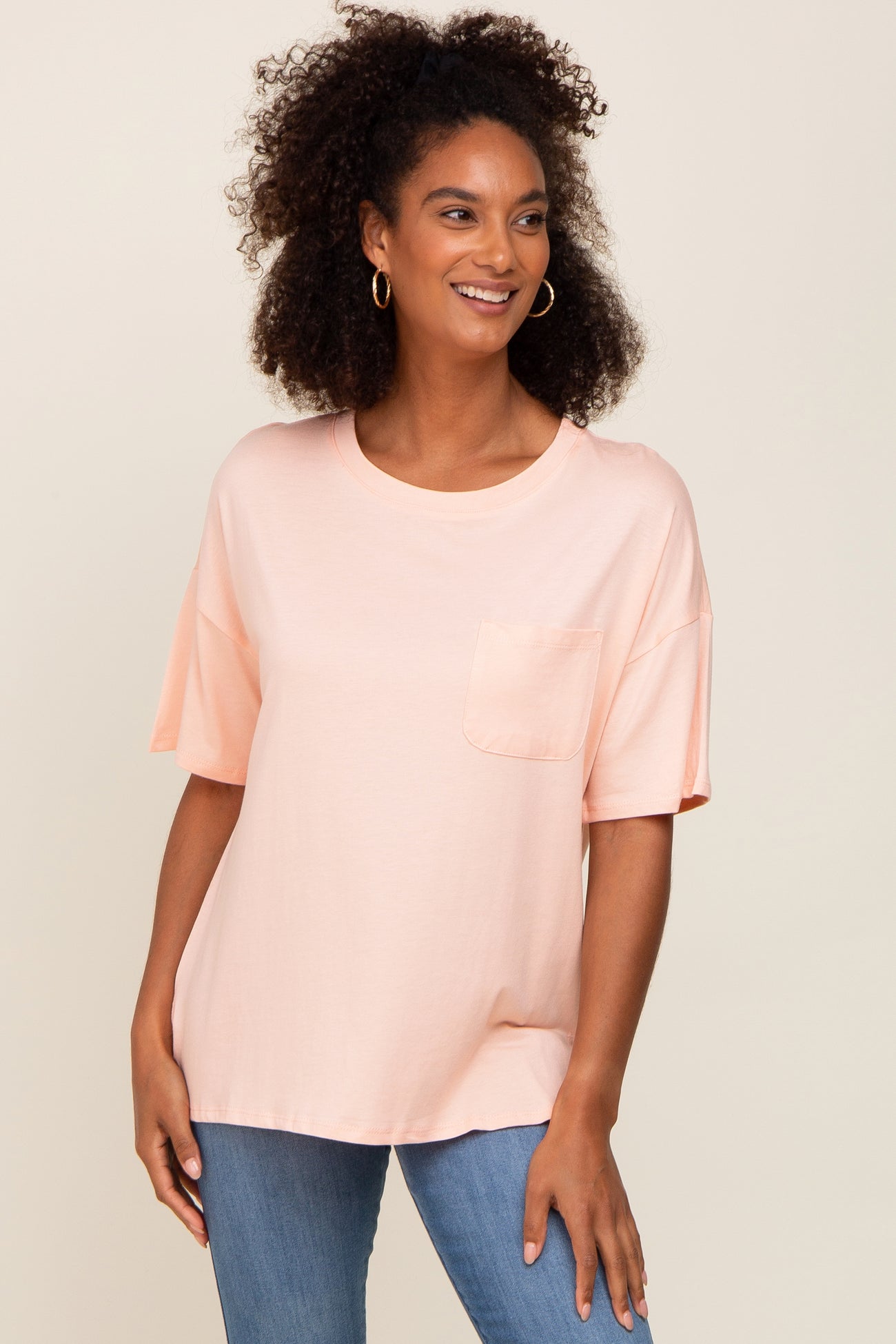 woman wearing a light peach oversized t-shirt with a chest pocket and short sleeves, paired with blue jeans