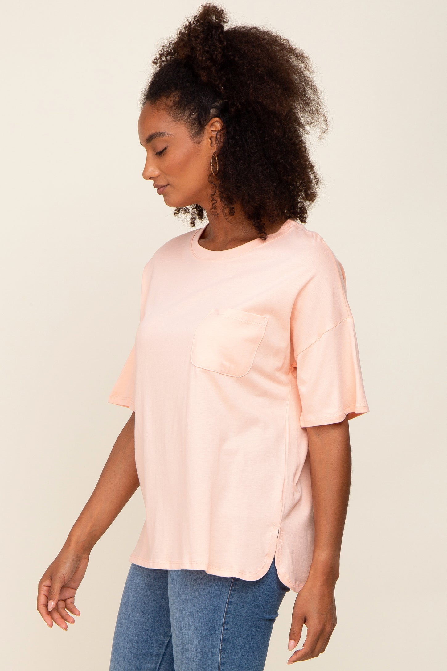 woman wearing a light pink short sleeve top with a pocket and side slits, paired with blue jeans