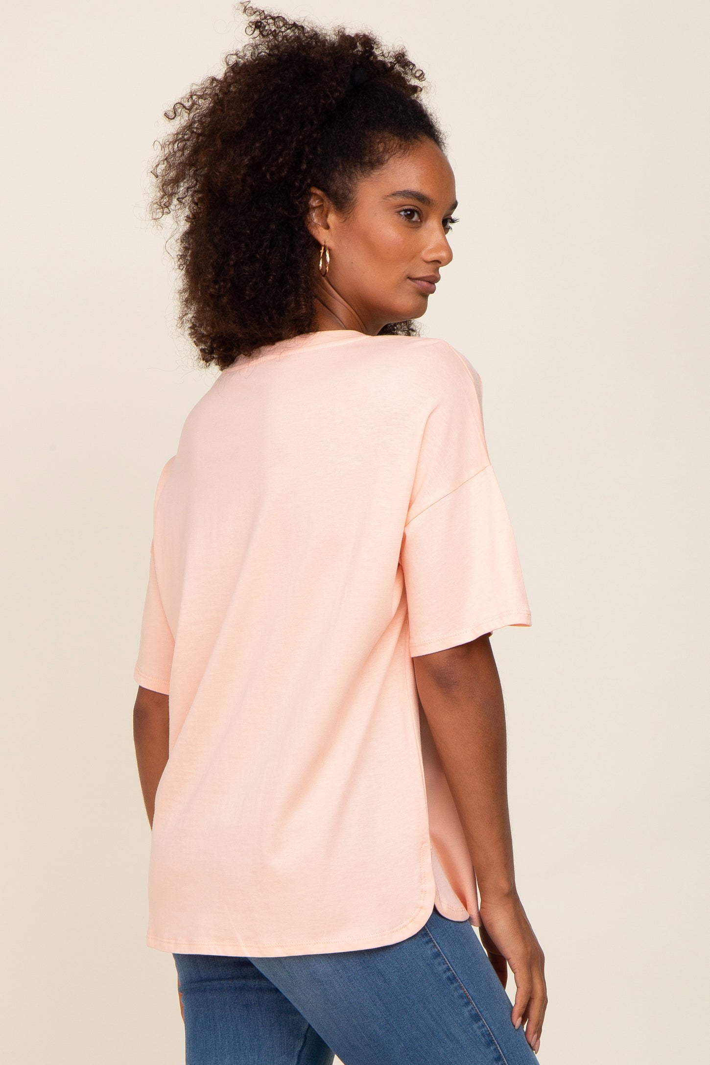 woman wearing a light pink short sleeve oversized t-shirt with a curved hem and back vent, shown from the side