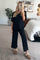 woman wearing a black lounge set with a loose top and wide-leg pants, standing in a cozy bedroom setting