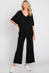 woman wearing a black v-neck oversized top and wide-leg black pants, paired with white sneakers