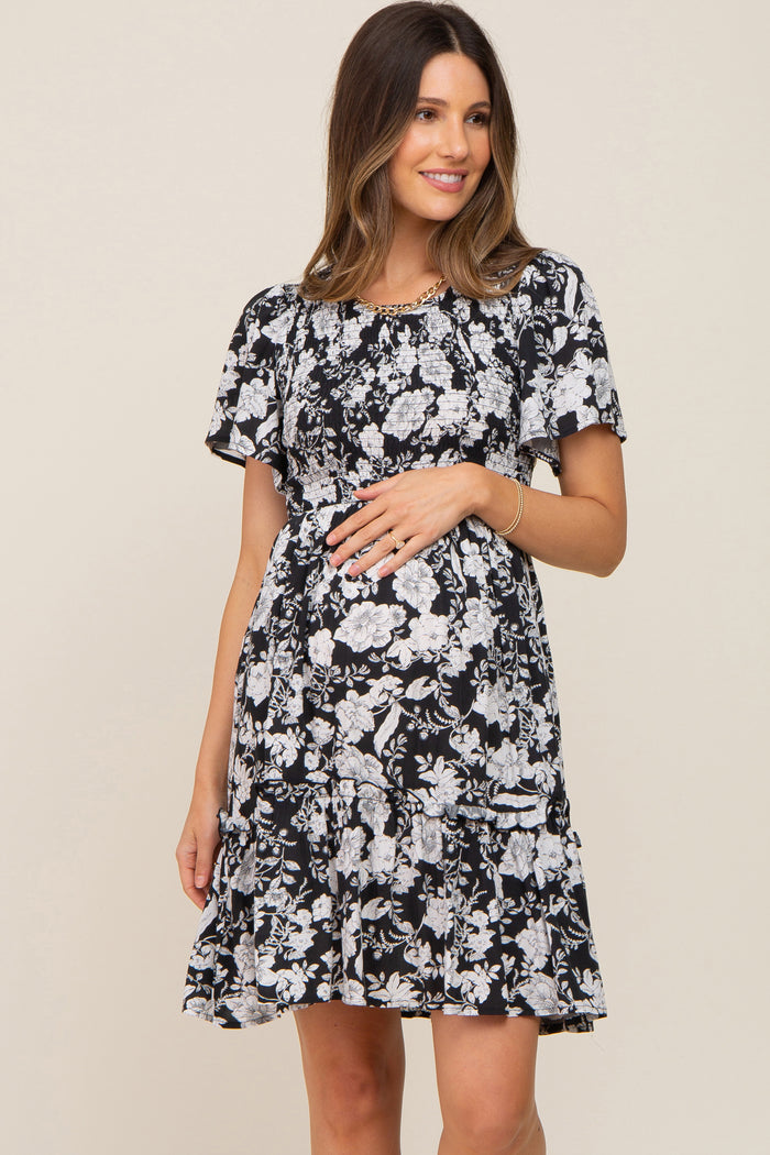 woman wearing a black floral maternity dress with short sleeves and ruffle hem, showing her baby bump