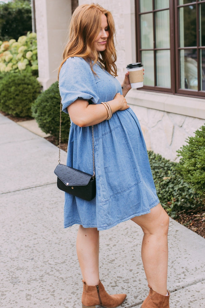 woman wearing a light blue maternity dress with short sleeves and a baby bump, holding a coffee cup