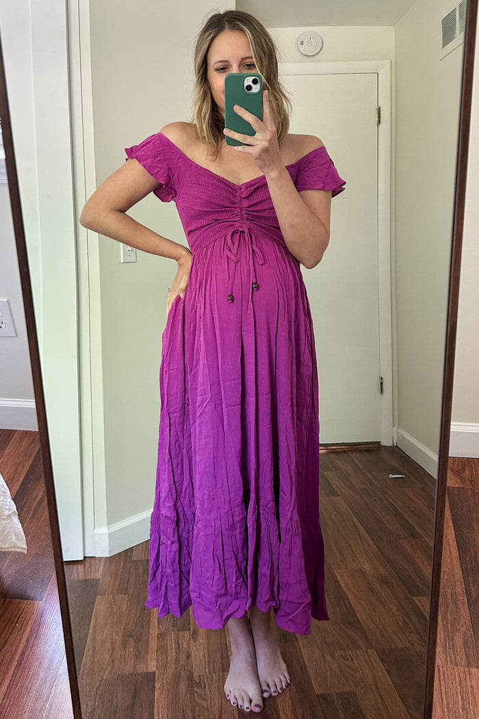 woman wearing a pink off-the-shoulder maternity dress with a tie front and a visible baby bump