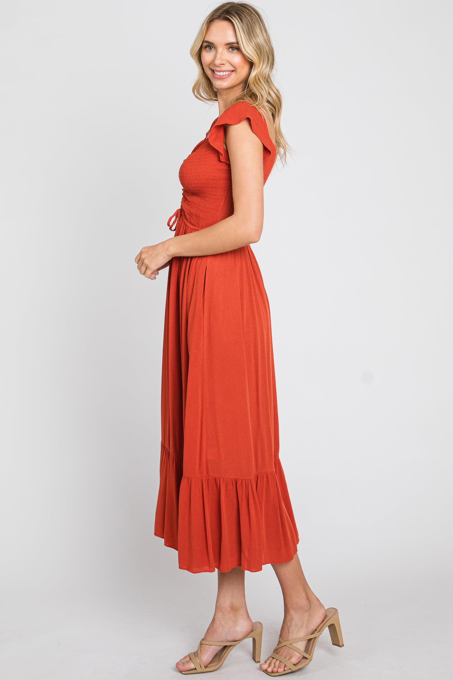 woman wearing a rust colored smocked midi dress with ruffle sleeves and a tiered skirt, styled with beige heeled sandals