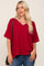 woman wearing a red v-neck oversized top with short sleeves and a pocket, paired with blue jeans