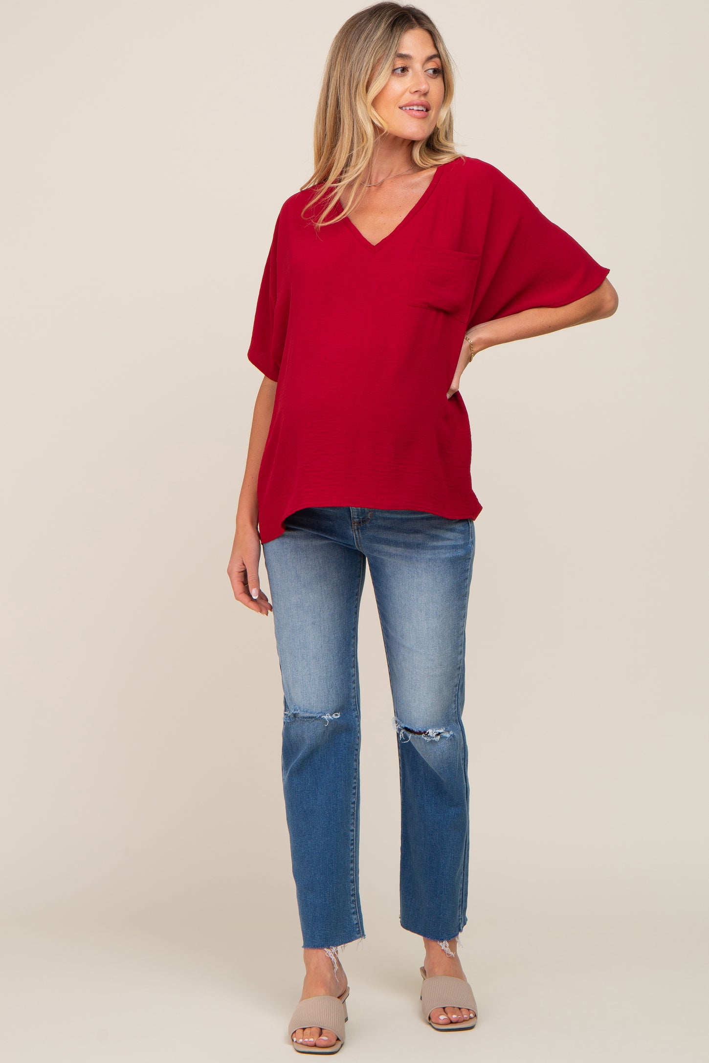woman wearing a red v-neck maternity top and distressed blue jeans with a visible baby bump