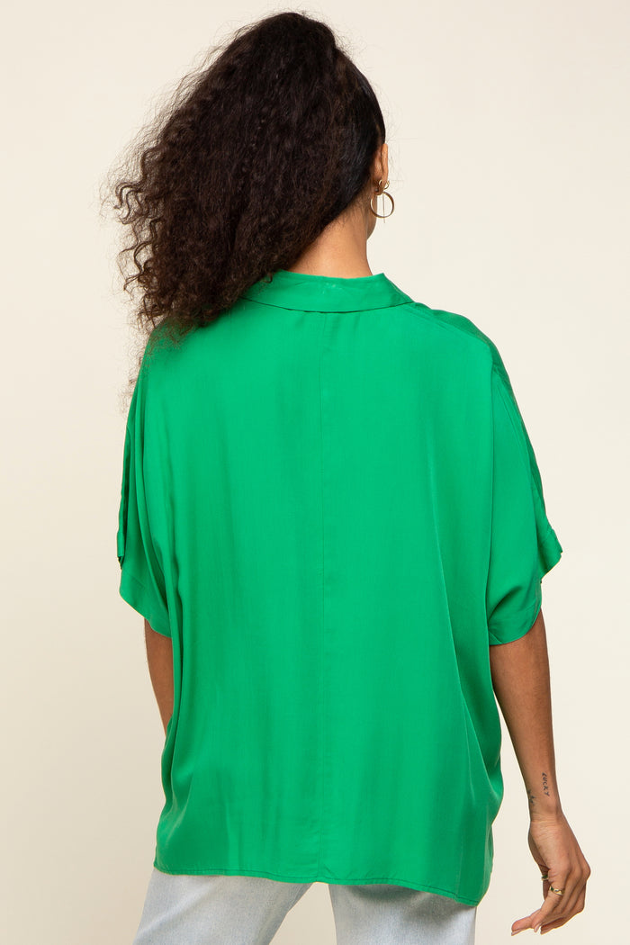 woman wearing a flowy green oversized blouse with short sleeves and a relaxed fit, viewed from the back