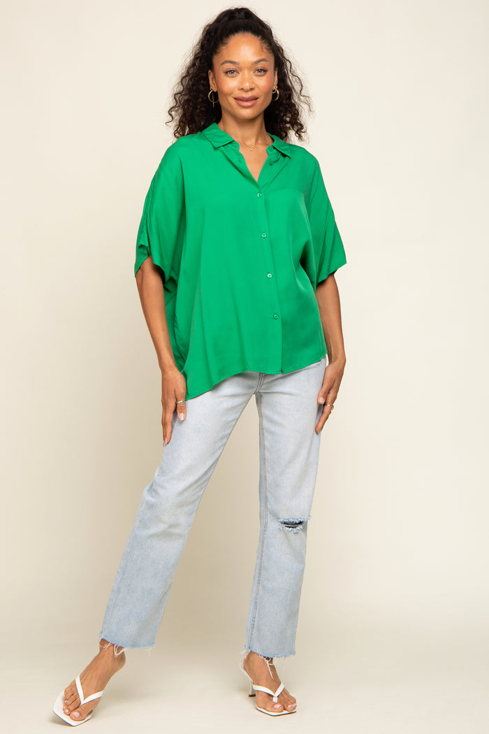 woman wearing a green oversized button-up shirt with rolled sleeves and light blue distressed jeans