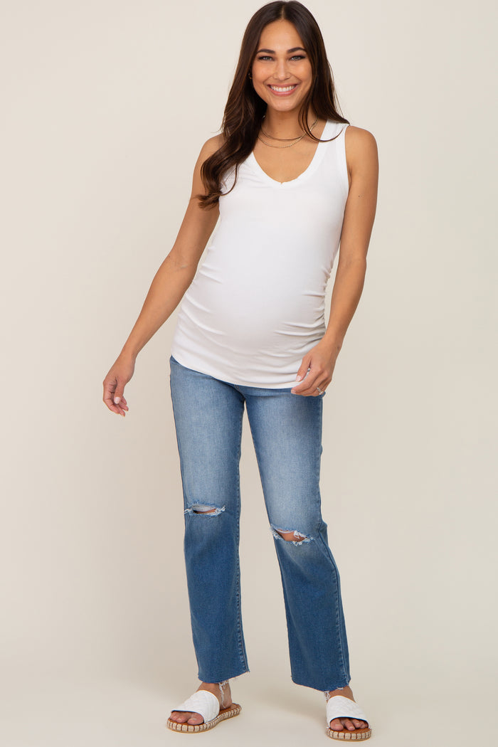 woman wearing a white maternity tank top and blue ripped flare jeans, showing her baby bump