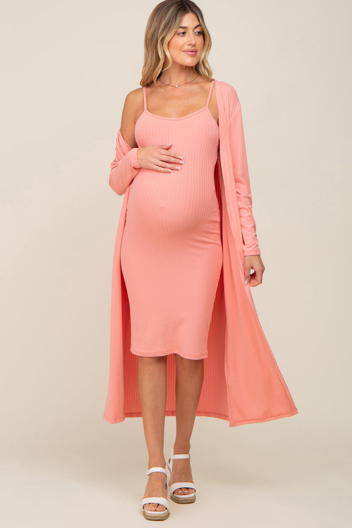 woman wearing a light pink maternity dress with spaghetti straps and a matching long cardigan, showing baby bump