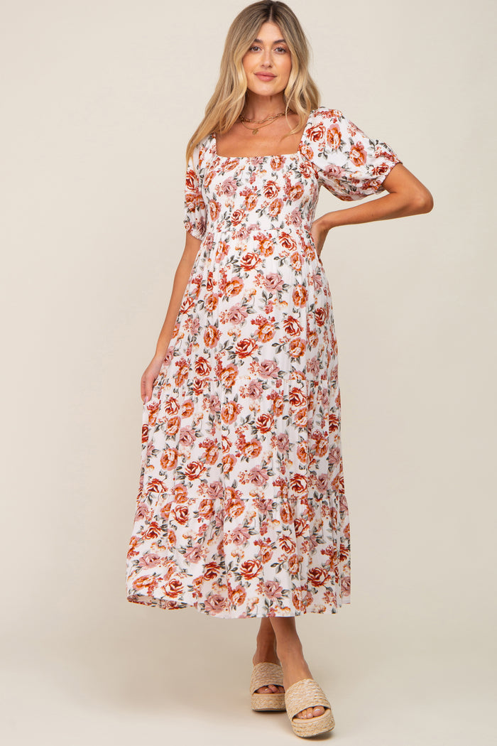 woman wearing a white floral smocked maternity midi dress with puff sleeves and tiered skirt