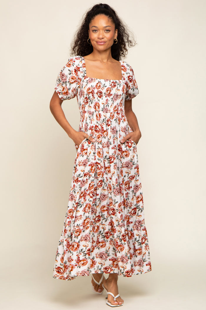 woman wearing a white floral maxi dress with puff sleeves and pockets, smiling at the camera