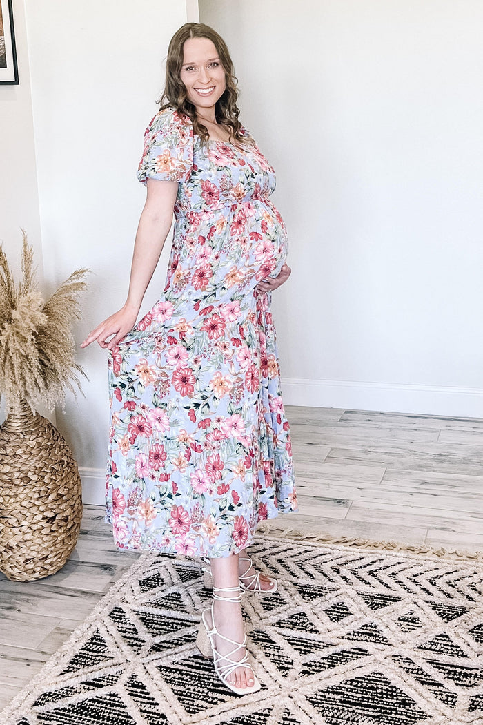pregnant woman in floral maternity maxi dress and white strappy sandals standing in a bright room