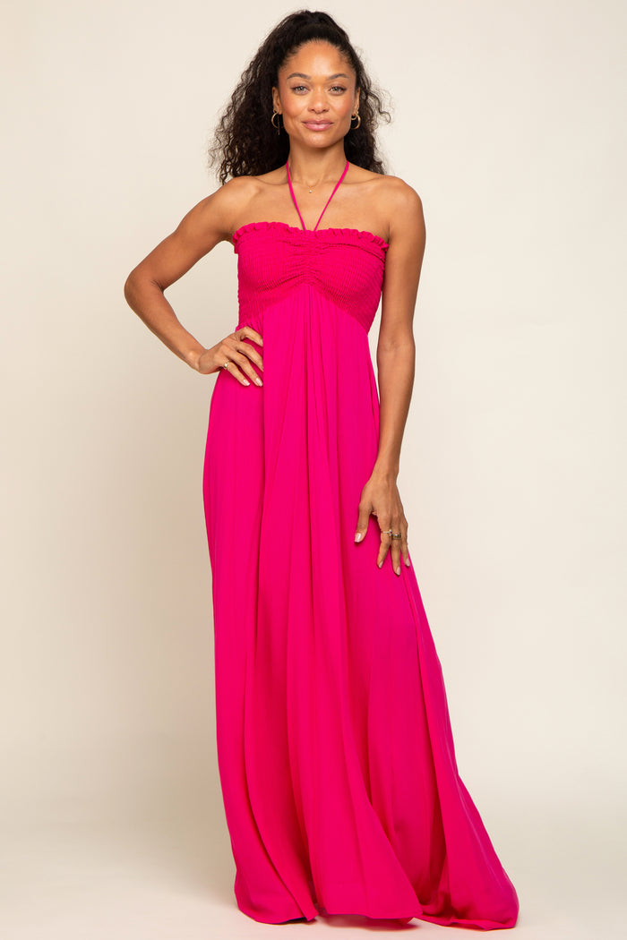Woman wearing a hot pink halter neck maxi dress with a smocked bodice and flowy skirt