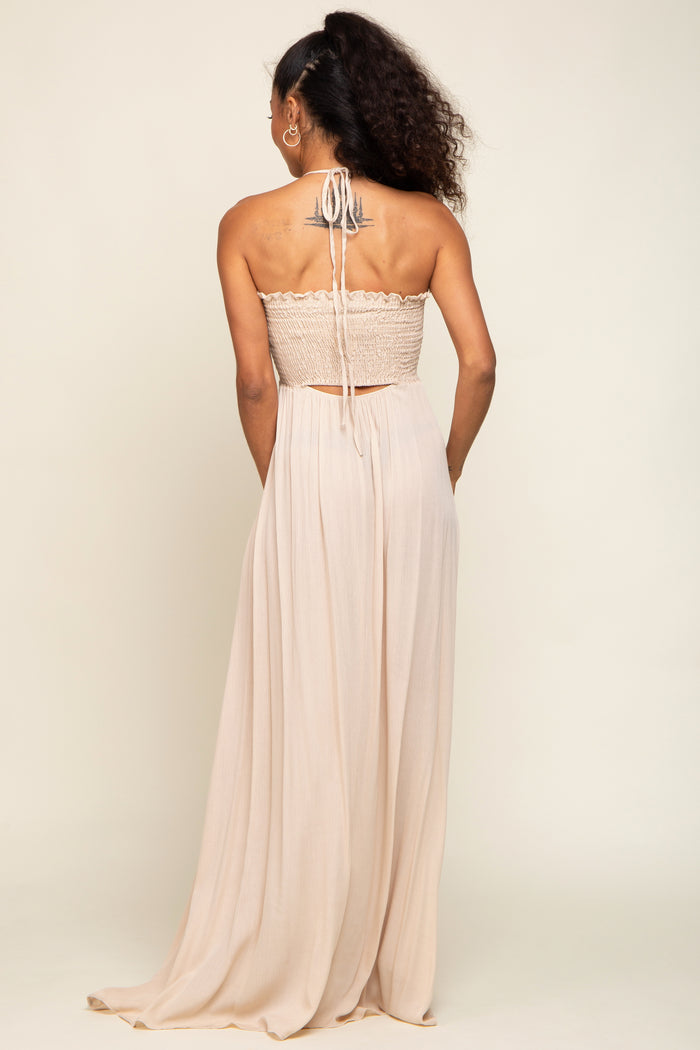 woman wearing a backless beige maxi dress with a smocked bodice and flowing skirt