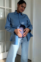woman wearing a light blue maternity shirt and holding her baby bump, paired with light denim jeans