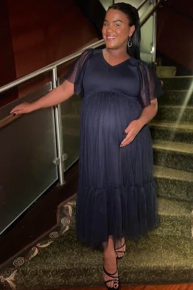 woman wearing a navy blue maternity dress with sheer puff sleeves and a tiered skirt, showcasing her baby bump