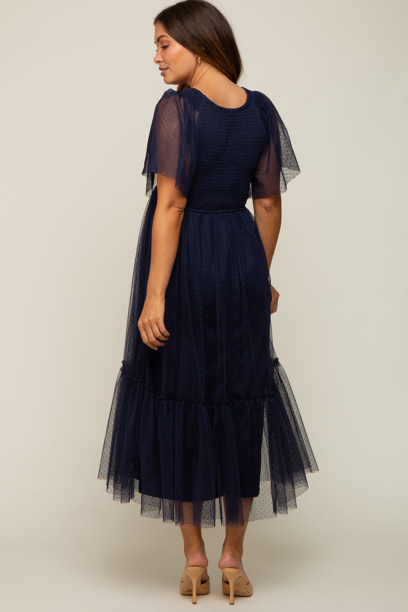 woman wearing a navy blue maternity midi dress with tulle sleeves and a tiered skirt, showing a baby bump from the back