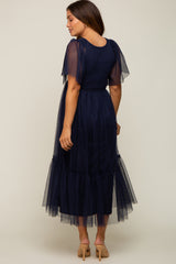 woman wearing a navy blue maternity midi dress with tulle sleeves and a tiered skirt, showing a baby bump from the back