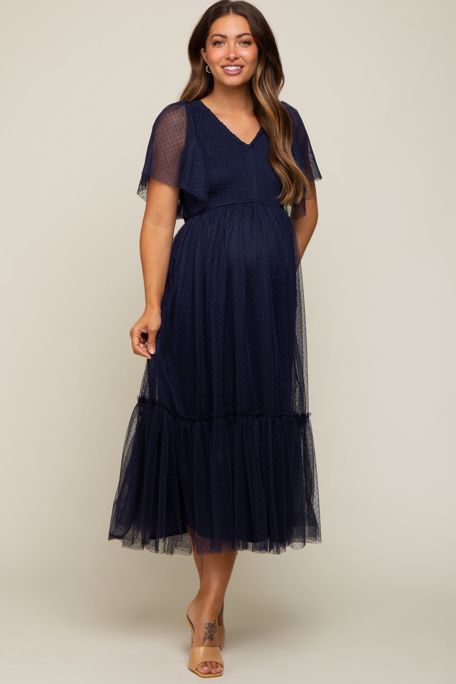 woman wearing a navy blue maternity dress with short flutter sleeves and a tiered tulle skirt, showing her baby bump