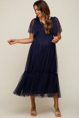 woman wearing a navy blue maternity maxi dress with short flutter sleeves and a tiered tulle skirt, showcasing her baby bump