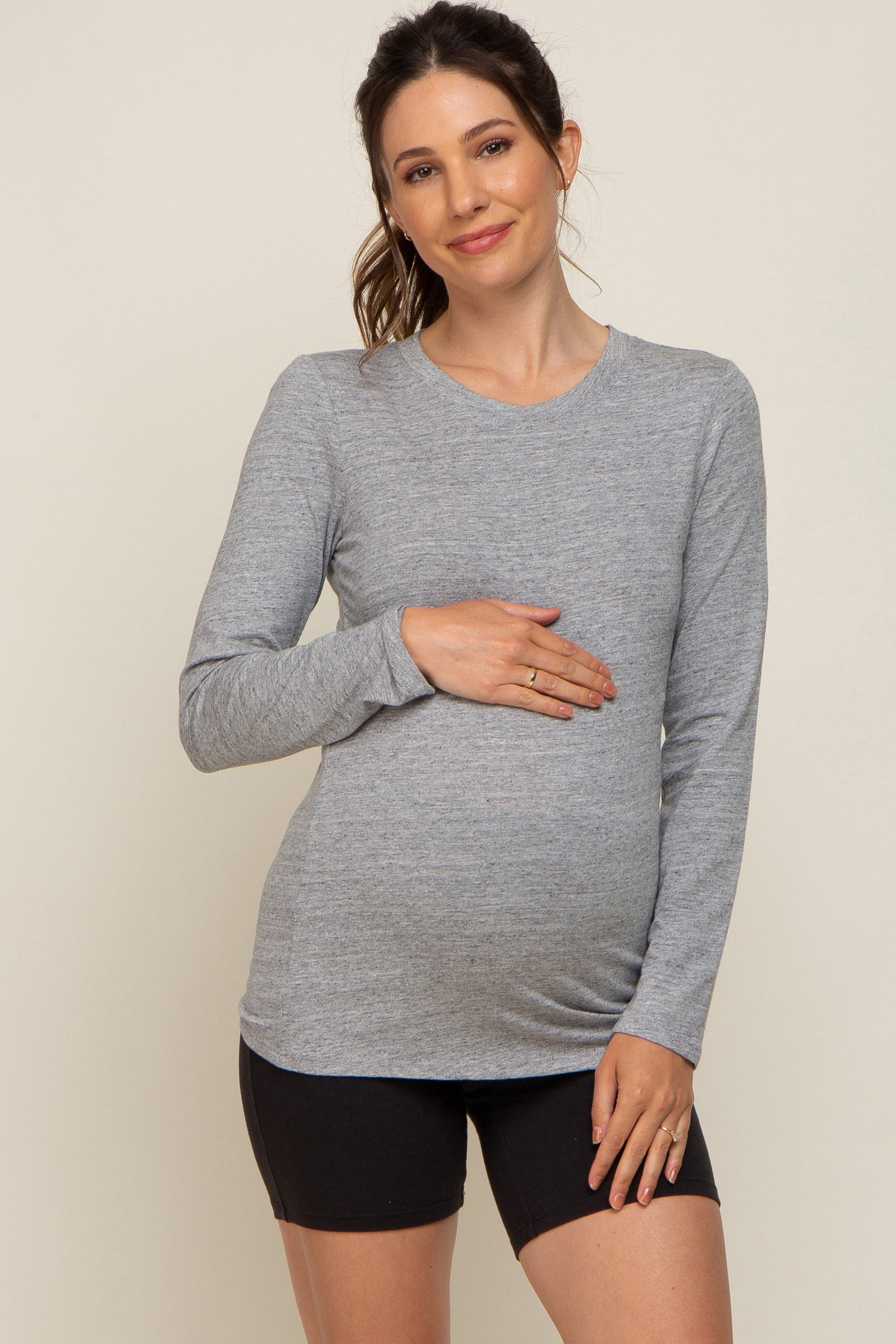 woman wearing a gray long sleeve maternity top and holding her baby bump, paired with black shorts