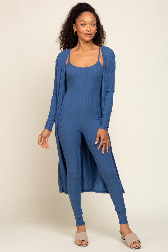 woman wearing a blue ribbed jumpsuit with a matching long cardigan and sandals, standing against a neutral backdrop