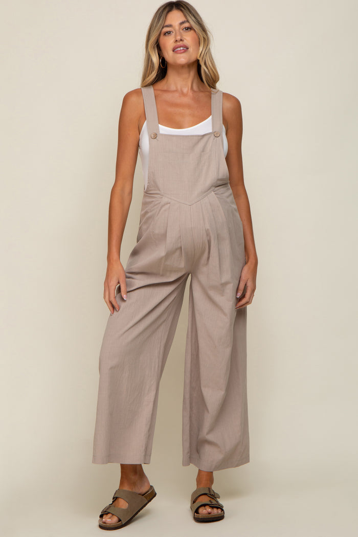 woman wearing a light brown maternity jumpsuit with wide legs and buttons, showcasing her baby bump.