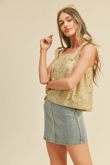 woman wearing a yellow floral sleeveless top with tie straps and a denim mini skirt