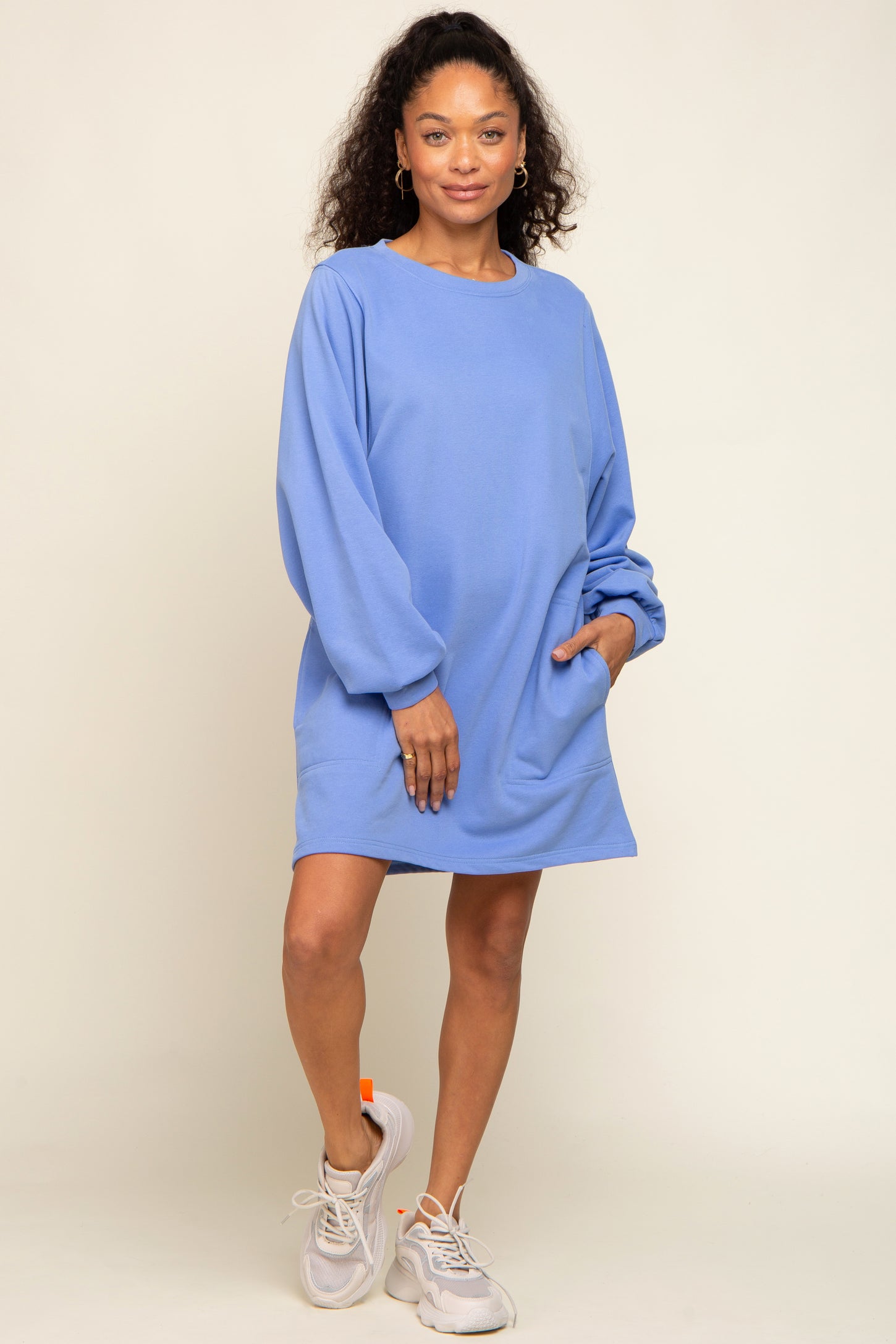 woman wearing a loose-fitting light blue sweatshirt dress with long sleeves and paired with white sneakers
