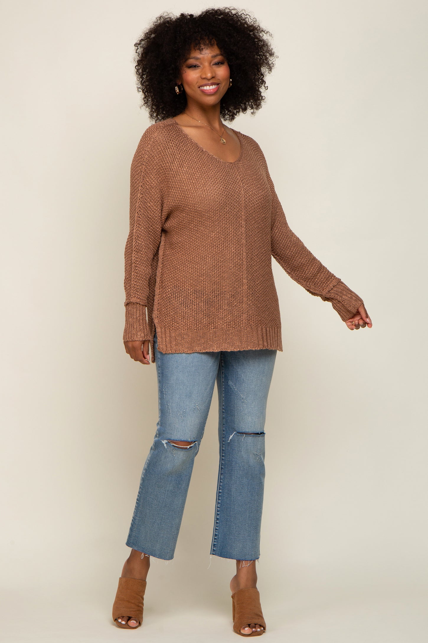 woman wearing a relaxed fit brown knit sweater and light blue distressed jeans, standing with a smile