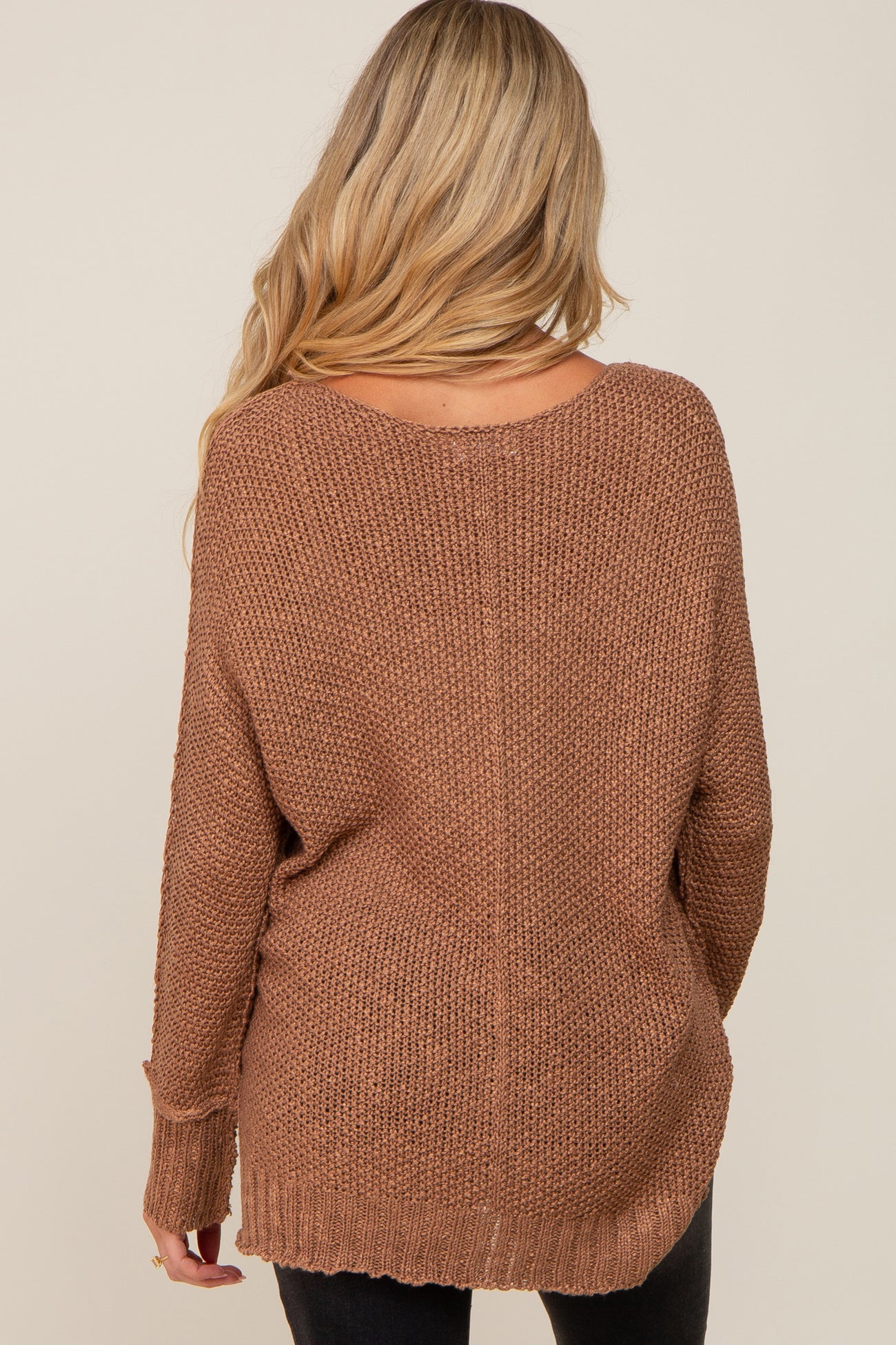 woman wearing a brown oversized maternity sweater with a loose fit and open back design