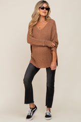 woman wearing a brown maternity knit sweater with a v-neck and side slits, paired with black cropped jeans and sunglasses